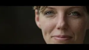 Close-up of a woman with short hair, smiling gently, showcasing bright blue eyes and a warm, inviting expression.