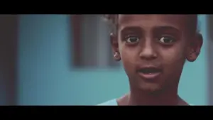 Young child with expressive eyes speaking in front of a soft blue background, capturing a moment of curiosity and emotion.