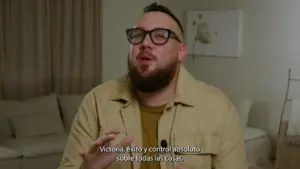 Man wearing glasses speaks passionately in a well-lit room, emphasizing themes of victory and control.