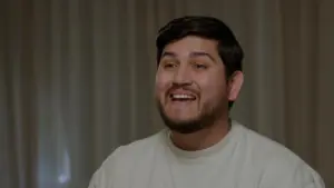 Smiling man in a casual white shirt, with warm lighting and a soft background, conveying a friendly and approachable demeanor.