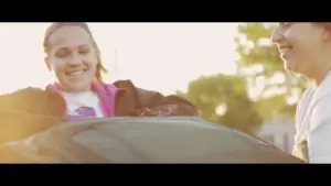 Two friends enjoying a sunny day, laughing and smiling as they clean a car together.