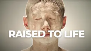 Young boy with a serene expression and a face covered in clay, emphasizing the phrase "RAISED TO LIFE" in bold letters.