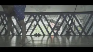 Person performing a handstand on a wooden floor with a geometric patterned railing in the background and natural light filtering in.