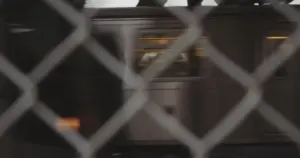 Subway train passing by a fence, highlighting urban transportation in a bustling city environment.