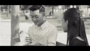 Young couple sharing a moment, smiling and engaged in conversation in a sunlit park setting. Black and white image.