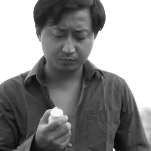 Man examining a small bottle in black and white, displaying a serious expression in a thoughtful outdoor setting.