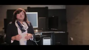 Businesswoman presenting in a modern office with computers and tech equipment in the background. Professional setting.