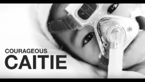 Child wearing a breathing mask, highlighting bravery and resilience, with the words "Courageous Caitie" prominently displayed.