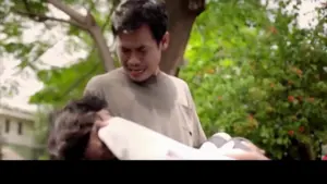 Man holding another person outdoors, expressing concern under a leafy tree with soft sunlight filtering through.