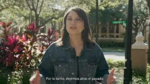 Woman in a denim jacket speaking outdoors, surrounded by lush greenery and colorful plants, conveying a message of moving forward.