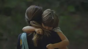 Woman embracing a child in a serene outdoor setting, showcasing love and comfort between them.