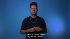 Man with short hair in a black shirt gestures confidently against a blue background while speaking.