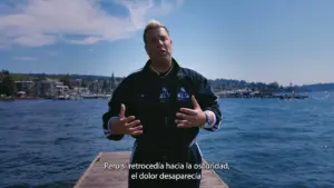 Person gesturing outdoors by a waterfront with a scenic view, discussing personal experiences and emotions.