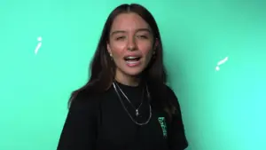 Young woman with long hair wearing a black t-shirt stands against a vibrant turquoise background, smiling confidently.