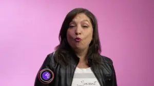 Woman in a leather jacket against a pink background, expressing confidence and joy with playful gestures.