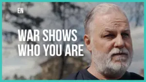 Close-up of a thoughtful older man with a gray beard, reflecting on the impact of war and personal identity.