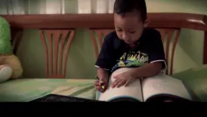 Child focused on drawing in a large book while seated on a bed, showcasing creativity and concentration in a cozy room.