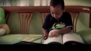 Young child sitting on a bed, focused on drawing in a large book with a colorful pencil. Bright, inviting room setting.