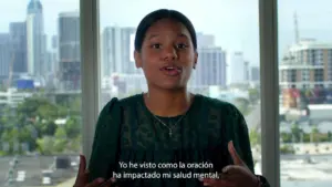 Young woman speaking passionately in front of a city skyline, sharing her experience about the impact of prayer on mental health.