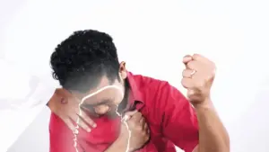 Young man in a red shirt clutches his chest in pain, expressing distress, against a white background.