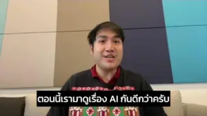 Young man in a colorful sweater speaking in front of a multicolored wall, discussing AI topics in Thai.