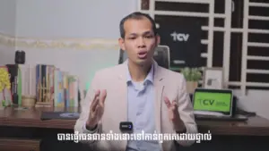 Man in a blazer speaking passionately in a modern office setting with a laptop and green logo in the background.