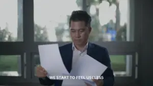 A man in a suit examines documents, reflecting on feelings of frustration and uselessness in a modern office setting.