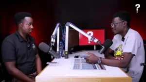 Two men discussing in a modern podcast studio with microphones and a vibrant red background.