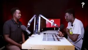 Two men sitting at a podcast studio table, engaged in conversation with microphones and sound equipment in a modern setting.