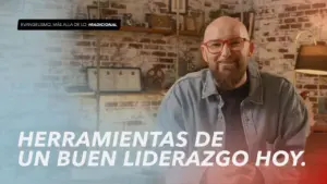 Smiling man in glasses discussing modern leadership tools against a brick wall backdrop.