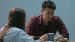 Man and woman sit at a table in an intense conversation, with coffee cups and a serious atmosphere in the room.