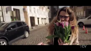 Woman joyfully holding a bouquet of tulips on a cobblestone street, showcasing a vibrant city atmosphere.