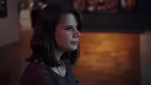 Young woman with a contemplative expression in an art gallery, illuminated by warm light.