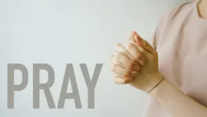 Person with clasped hands in prayer, with the word "PRAY" displayed prominently in the background.