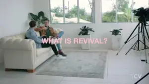 Two people sitting on a sofa in a bright room discussing "What is Revival?" with plants and a camera in the background.