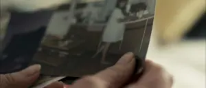 A person holding a vintage photo of a woman in a white dress standing at a counter in a nostalgic setting.