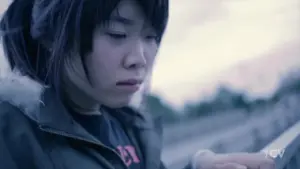 Young woman with dark hair, focused on her phone outdoors, captured in a soft, moody atmosphere.