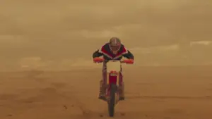 A motocross rider performs a jump in a sandy landscape under an orange sky, showcasing thrilling action and adventure.