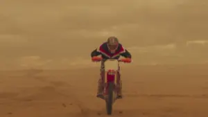 A motorcyclist performs a daring jump over sandy terrain under a dramatic sky, showcasing thrilling off-road action.