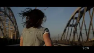 Woman running on a bridge at sunset, with her hair flowing in the wind and a clear sky in the background.