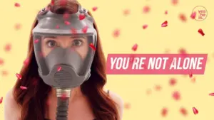 Woman in a gas mask surrounded by rose petals, conveying a message of support with "YOU'RE NOT ALONE" text.