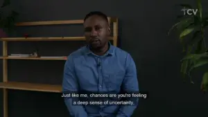 A man in a blue shirt sitting thoughtfully in front of a minimalist bookshelf, expressing feelings of uncertainty.