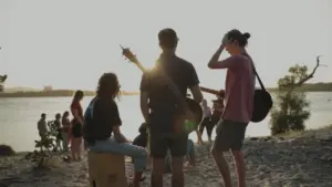 Group of friends enjoying a lakeside jam session during sunset, with instruments and a scenic backdrop.