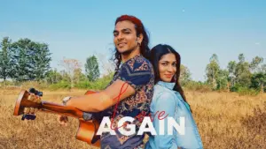 Couple standing back-to-back in a field, holding a guitar, with a clear blue sky and trees in the background.