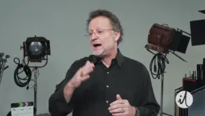 Man in a black shirt speaking, with studio lights and equipment in the background, creating a professional atmosphere.