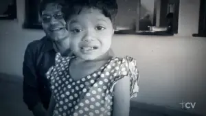 Smiling man with glasses and young girl in polka dot dress pose together, captured in a nostalgic black-and-white photo.