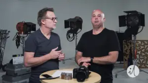 Two male photographers discussing equipment in a studio setting with cameras and lighting in the background.