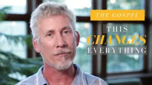 Man with light hair and beard speaking, with text overlay: "The Gospel This Changes Everything" against a blurred background.