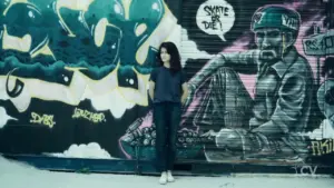 Young woman standing against vibrant graffiti mural featuring skateboarding themes and urban art.