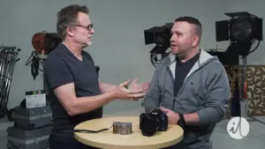 Two men discussing photography techniques at a studio with cameras and lighting equipment in the background.